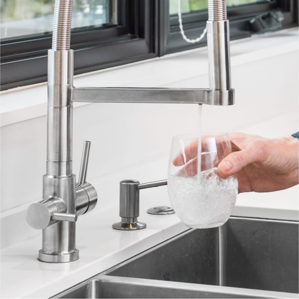 Seltzatap in a white designer kitchen. A man's hand holds a glass underneath the fizzy water spout.